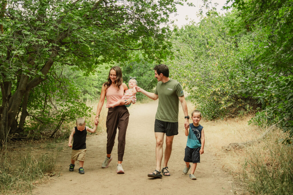Natalie Kravat walking outdoors on a wooded trail with her husband and three young children